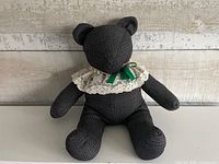 Front view of black textured handmade teddy bear with lace collar and green bow