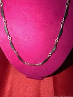 Full view of silver tone necklace displayed on bust showing wavy bar links and connectors