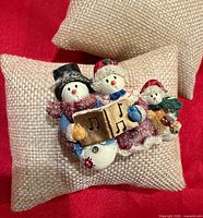 Front view of painted stone brooch with three snowmen carollers and glitter accents