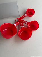 Four red plastic Betty Crocker measuring cups spread out on ring