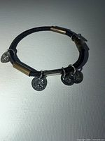 Full view of stretch bracelet showing cord, brass-tone tubes and dangling coin charms