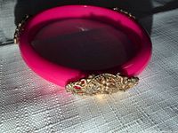 Entire hot pink plastic bangle showing one gold-tone filigree accent