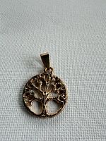 Front view of gold tone Tree of Life pendant on fabric background