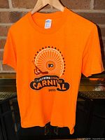 Front view of orange Flyers Carnival 2023 T-shirt on hanger