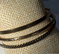 Three bangles on display cylinder, showing plain, scalloped, and textured designs