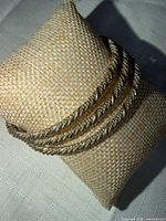 Three gold-tone rope-twist bangles displayed on fabric cushion