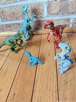 Five assorted plastic dinosaur figures on wood floor