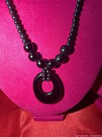 Black glass bead choker necklace with oval pendant displayed on stand