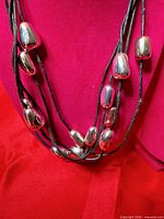 Necklace draped to show multi-strand cords and silver-tone bean beads