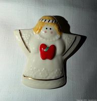 front view of white ceramic angel brooch showing red heart and gold trim