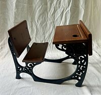 Front three-quarter view showing desk, seat, backrest, cast metal frame, wood surfaces