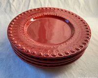 Stack of four red Fantasy pattern dinner plates showing molded border and glossy finish