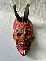 Front view of carved wood diablo mask with painted motifs and attached horns