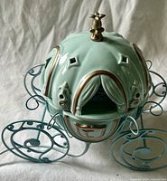 Full view of ceramic Cinderella carriage warmer showing metal wheels and lid