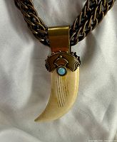 Close view of pendant showing brass cap, turquoise cabochon and bone-tone tooth