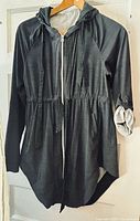 Front view of charcoal hooded jacket on hanger showing full zipper, hood drawstrings, curved hem