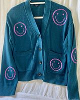 Front view of cardigan showing color, button front, pockets, smiley faces