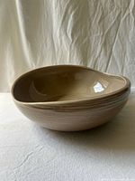 Oblique view of stoneware serving bowl showing asymmetrical rim, interior glaze, and exterior stripe texture
