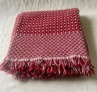 Folded red and white handwoven textile showing overall color and fringe