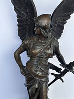 Front three-quarter view of bronze winged female figure showing sword, drapery and knee scrape