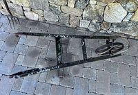 Full view of metal farm cart frame lying on stone pavers showing overall structure and wear