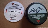 Top view of signed puck beside authenticity card showing signatures, logos and text