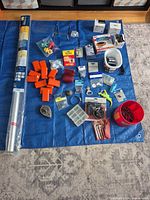 Full lot overview on blue tarp showing insulation roll, hardware items