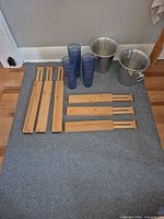 All items laid out: 4 long and 3 short bamboo dividers, stack of blue tumblers, two stainless buckets