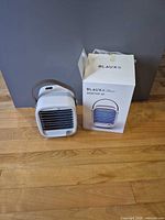 Air conditioner beside original box showing front grille and strap