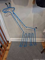 Full view of blue giraffe-shaped coat rack leaning against wall