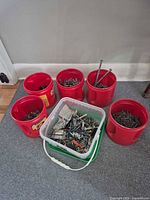 Five red pails and one clear pail filled with assorted fasteners