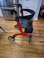 Side profile of red Drive Nitro rollator showing frame, wheels, seat folded up and storage pouch