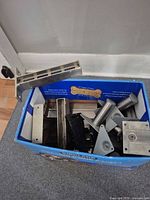 Box containing assorted stainless, grey and black metal brackets and legs
