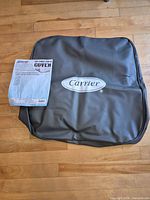 Gray vinyl Carrier-logo air conditioner cover with paperwork resting on top
