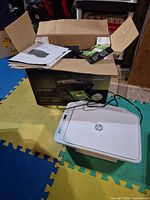 Printer on floor with power cable, manuals and original box visible