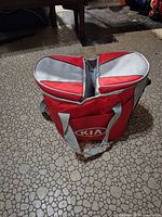 Cooler bag exterior showing red body, gray handles, Kia logo, dual-compartment top