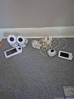Two Project Nursery cameras, one Project Nursery parent unit, one Summer camera, one Summer parent unit, power adapters and cables on floor