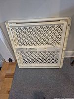 Front view of folded off-white plastic pressure-mount safety gate