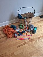 Yarn skeins, basket, needles, hook displayed on floor
