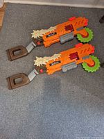 Two identical Zuru X-Shot blasters on carpet, full view