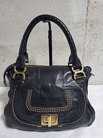 Front view of black Chloé Marcie bag showing turn-lock pocket, stitching, handles, hardware