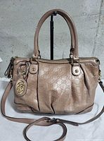 Front exterior view of Gucci metallic light pink Guccissima Sukey Medium Tote with handles, shoulder strap, GG charm