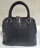 Front view of Gucci Microguccissima black leather handbag showing rolled handles and gold-tone hardware