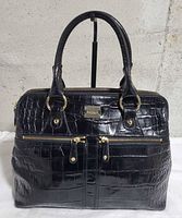 Front view showing croc texture, front zip pockets, handles, hardware, logo plaque