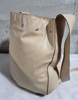 Side view of beige leather tote showing strap and eyelets