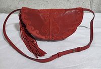 Front view of red embroidered leather croissant bag with tassel and strap