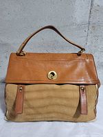 Front view showing leather flap, embossed suede body, turn-lock and top handle