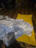 Assorted linens spread on floor showing snowman pillowcase, yellow quilted cloth, floral tablecloths