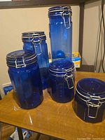 Front view of all five blue glass canisters showing size gradation and wire clamp lids