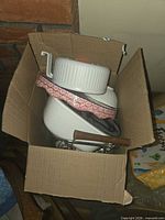 Box containing stacked white enamel cookware items, visible wooden handle and metal rack